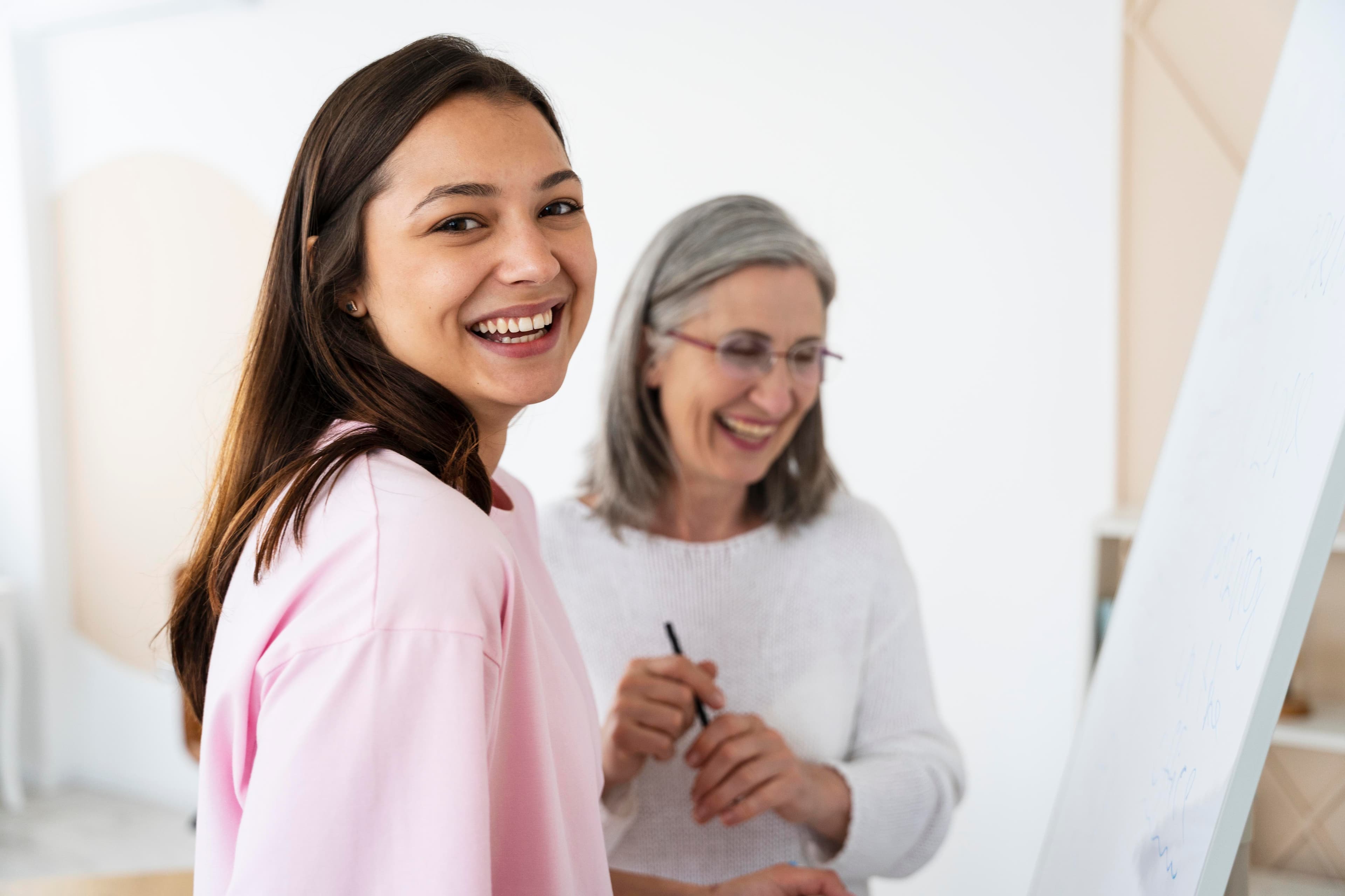 Young woman smiling at the camera next to an older woman in front of a whiteboard