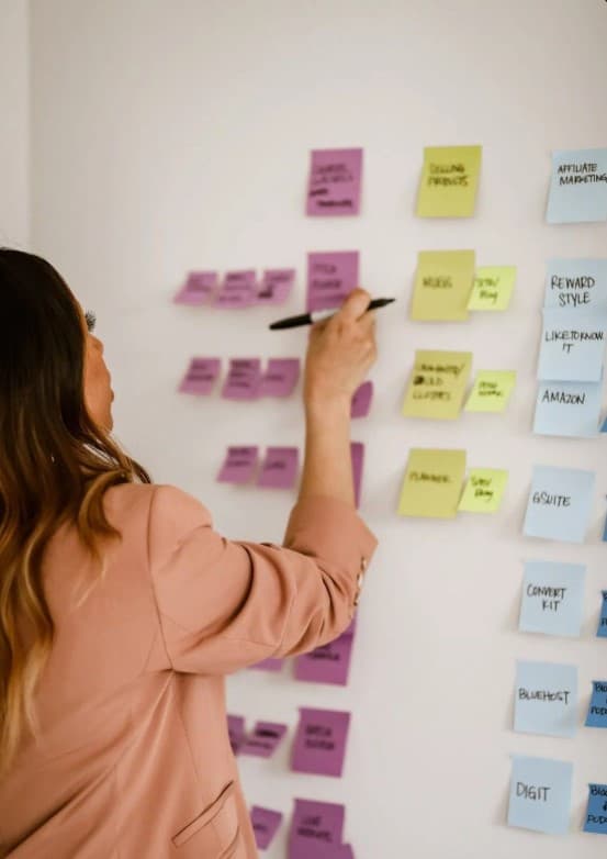 Woman seen from behind arranging colorful sticky notes on a wall