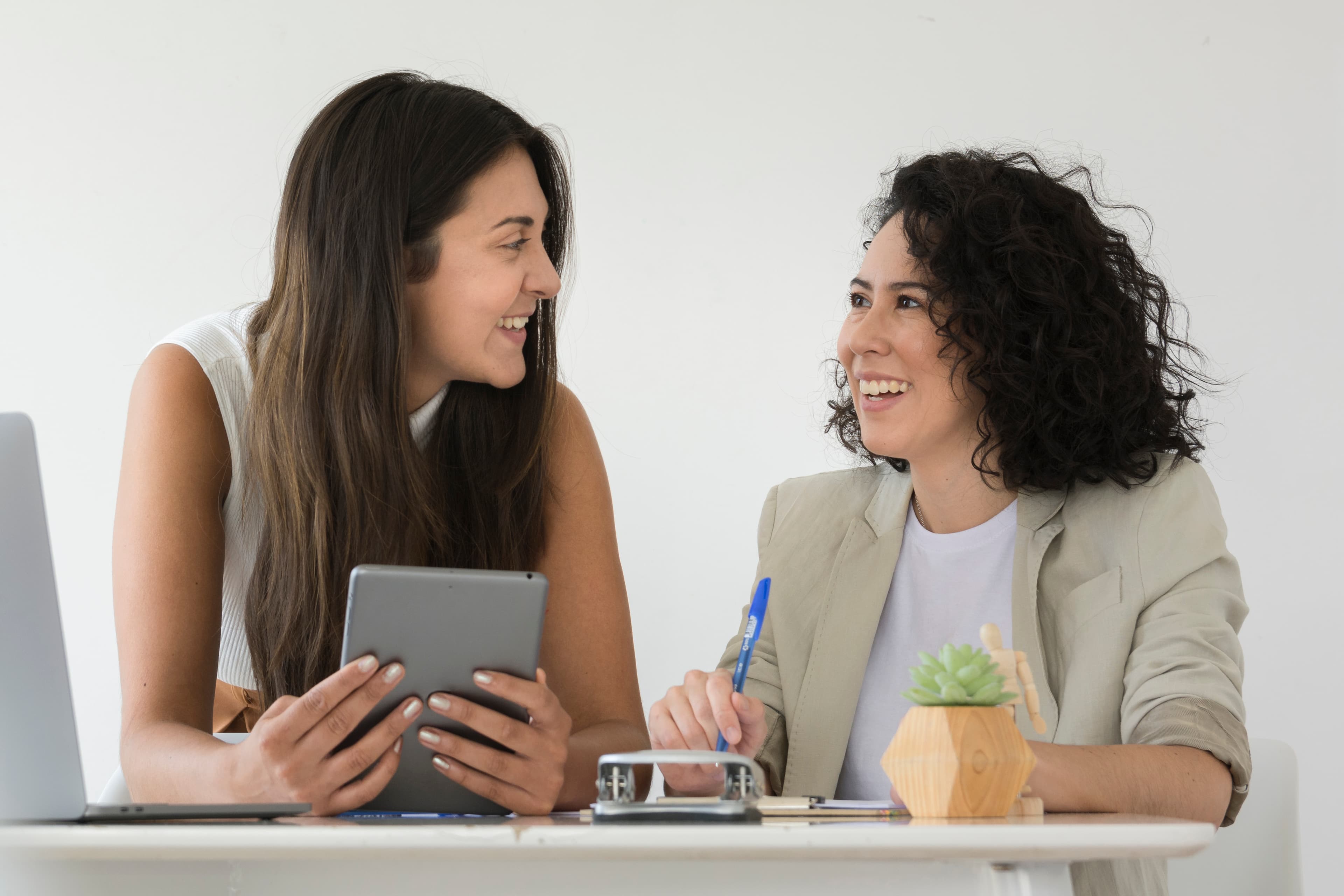 Two smiling women having a mentoring session in an office, one holding a tablet and the other taking notes